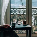 Kobieta w okularach odpoczywa przy stole z laptopem przy oknie