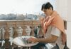 Jak urządzić balkon jako mini strefę relaksu i pracy w jednym Mężczyzna pracuje przy laptopie i pije kawę na miejskim balkonie