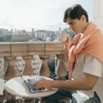 Mężczyzna pracuje przy laptopie i pije kawę na miejskim balkonie